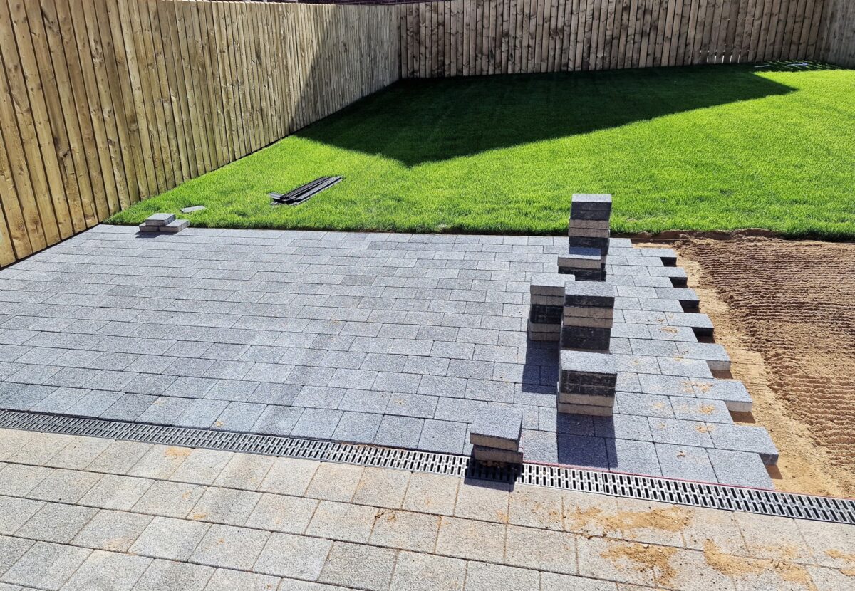 Grey block paving being laid beside a new lawn and fence